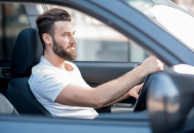 Hombre con barba manejando en carretera cubierto por su seguro de auto